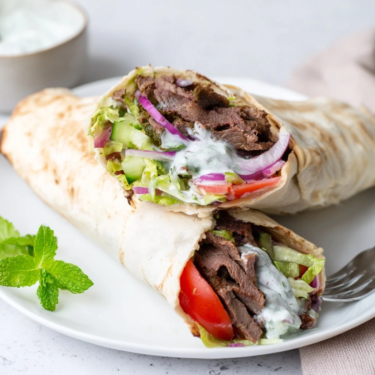 Tender beef shawarma wraps filled with creamy yogurt sauce and fresh vegetables.  
