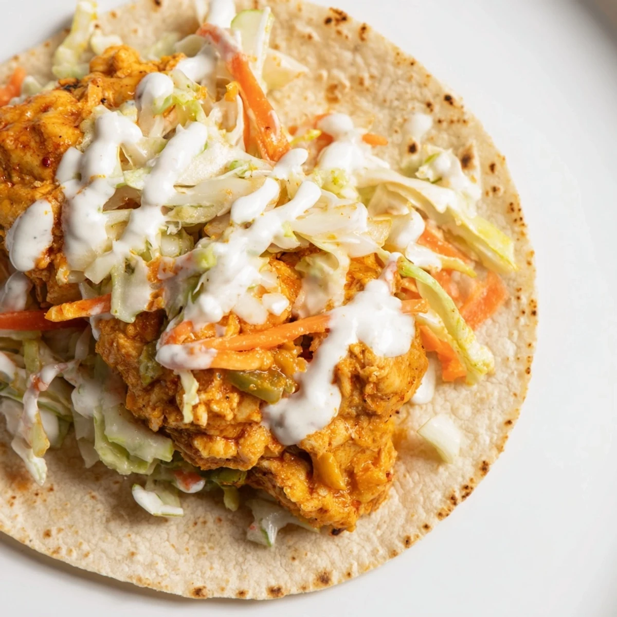A plate of Buffalo Chicken Smash Burger Tacos, dripping with sauce and topped with creamy slaw.