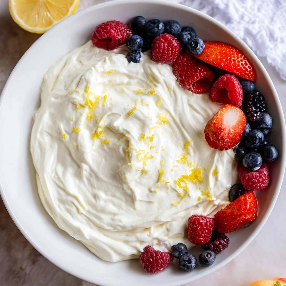 A close-up shot of the creamy, fluffy cream cheese fruit dip with fresh, colorful berries arranged around it.