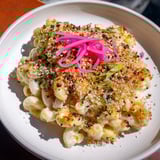 A comforting bowl of Katsu Curry Mac & Cheese, drizzled with savory sauce and herbs.