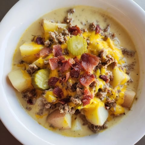 Crockpot Cheeseburger Soup overflowing a bowl, topped with shredded cheddar, crispy bacon, and pickles.