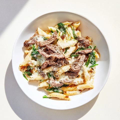 Steak & Spinach Artichoke Pasta Bake bubbling with golden mozzarella, served in a casserole dish.