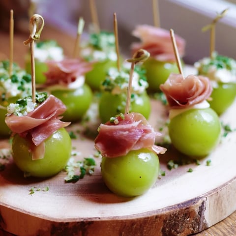 Fresh Mistletoe Kissing Ball appetizer with creamy cheese balls, grapes, and prosciutto, ready to serve.