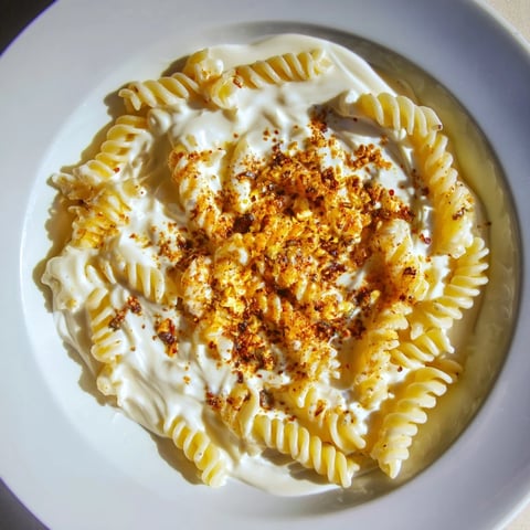 A bowl of Turkish Yogurt Pasta, swirled with creamy sauce, garnished with herbs and spiced butter.